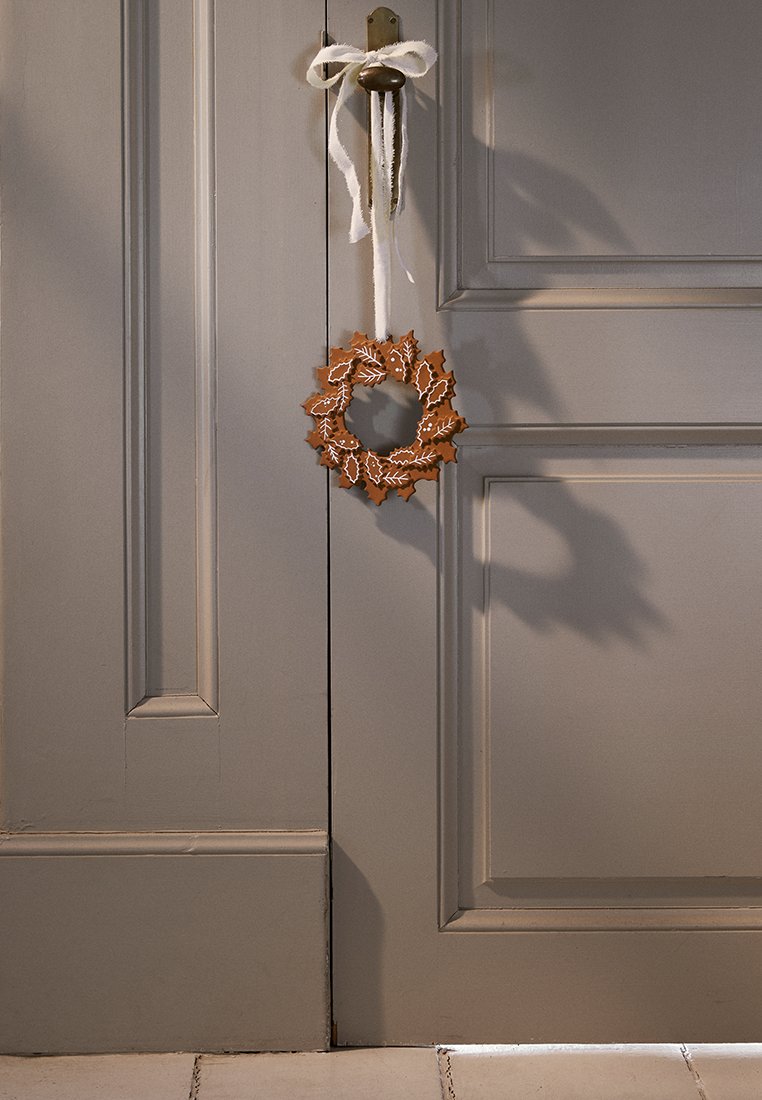 Brauner dekorativer Kranz mit Blattmuster, der an einem Band an einer grauen Tür hängt, die vertikale Wandverkleidung und einen Türknauf aufweist.