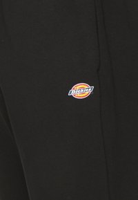 Pantaloni negri cu o textură netedă, având un patch colorat cu logo-ul "Dickies" pe lateral. Design simplu, drept, fără accente suplimentare.