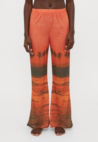 Pantalones de chándal acampanados en naranja con un gráfico de puesta de sol y palmera. Textura suave y cinturilla elástica para mayor comodidad.