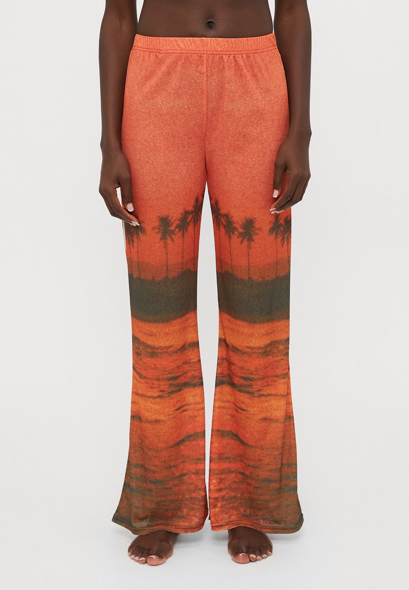 Pantalones de chándal acampanados en naranja con un gráfico de puesta de sol y palmera. Textura suave y cinturilla elástica para mayor comodidad.