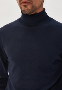 Pulover turtleneck de culoare albastru marin, realizat dintr-un material moale, tricotat, cu o croială ajustată și detalii ribbate la guler și la manșete.