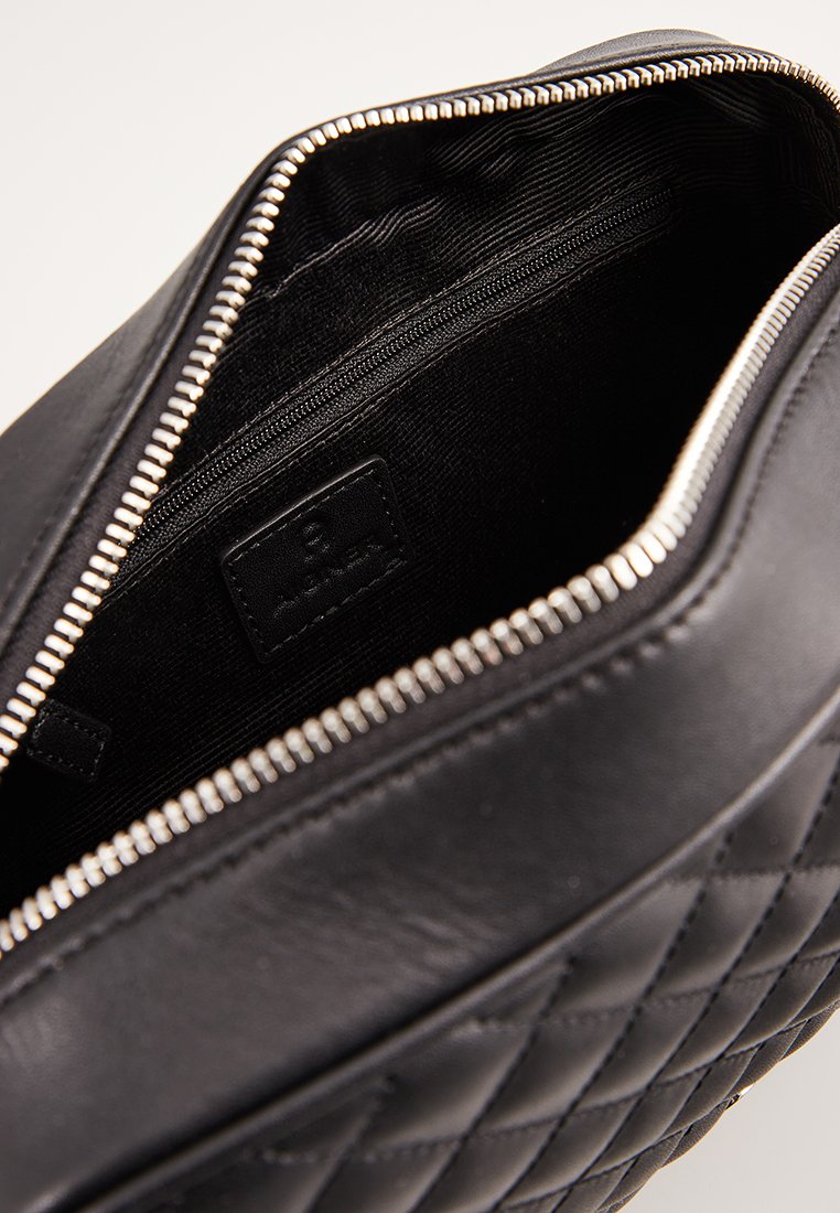 Schwarze Lederhandtasche mit gestepptem Design, silbernem Reißverschluss und einem mit Stoff ausgekleideten Innenraum mit einer kleinen Reißverschlusstasche.