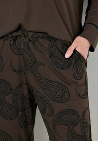 Pantaloni marroni con un motivo paisley nero, vita con cordoncino e tasche laterali. Tessuto morbido con una texture liscia. Design casual.