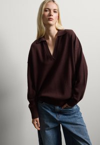Pull en tricot brun oversize avec un col en V, assorti à un jean en denim bleu ample. Texture légère et coupe décontractée.