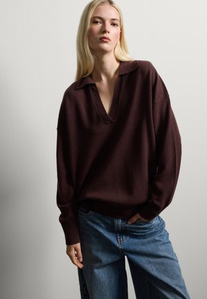 Pull en tricot brun oversize avec un col en V, assorti à un jean en denim bleu ample. Texture légère et coupe décontractée.