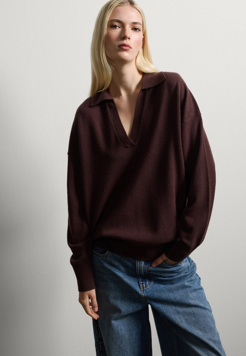 Pull en tricot brun oversize avec un col en V, assorti à un jean en denim bleu ample. Texture légère et coupe décontractée.