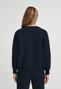 Svart tröja i ett mjukt material med avslappnad passform, sänkta axlar och ribbade ärmslut och nederkant för en bekväm look.