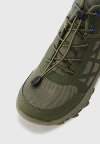 Shoe verde para atividades ao ar livre, com parte superior em malha e sintético, superfície texturada, cordões elásticos ajustáveis com botão de regulação e biqueira reforçada.