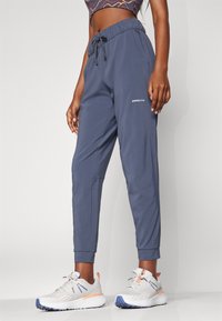 Navy lightweight joggers with an elastic waistband, drawstring, side pockets, and Patagonia logo on the lower leg. Paired with gray running shoes.