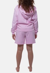 Roze bijpassende hoodie en short set gemaakt van zachte stof. De hoodie heeft een capuchon en ribgebreide manchetten, terwijl de shorts een gezoomde rand hebben.