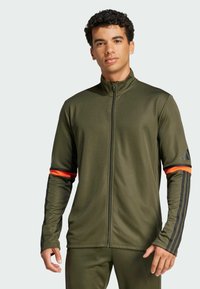 Olive green athletic jacket with high collar, front zipper, and black stripes on sleeves, featuring orange accents on cuffs.