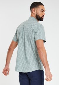 Kurzärmliges, mintgrünes Hemd mit Knöpfen, das ein kleines, weißes Blumenmuster aufweist und eine lässige Passform hat, mit geradem Saum und Rückenfalte.