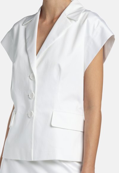 Sacou alb fără mâneci, cu rever larg, trei nasturi pe față și buzunare cu clapetă, purtat pe torsul unei persoane.