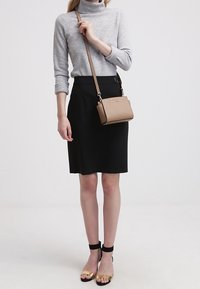 Borsa a tracolla in pelle marrone chiaro con hardware dorato e design strutturato, abbinata a un outfit composto da un maglione grigio e una gonna nera.