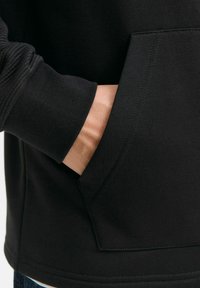 Zwarte sweatshirt met een geribbelde mouwmanchet en een zijzak. De stof lijkt soepel met nette stikdetails.