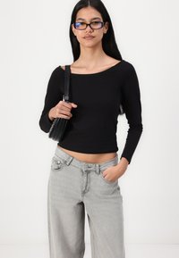 Black long-sleeve cropped top with a round neckline paired with light gray wide-leg jeans. Model holds a small black handbag.