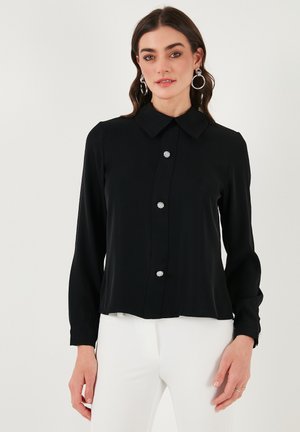Black blouse featuring a collar, long sleeves, and a button placket adorned with decorative round buttons. Smooth fabric with a tailored fit.