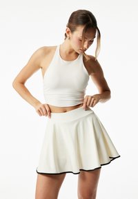 Valkoinen halterneck crop top yhdistetty valkoiseen skater-hameeseen, jossa on musta helma. Tasainen rakenne, jossa on tiukka vyötärö ja flare-muotoilu.