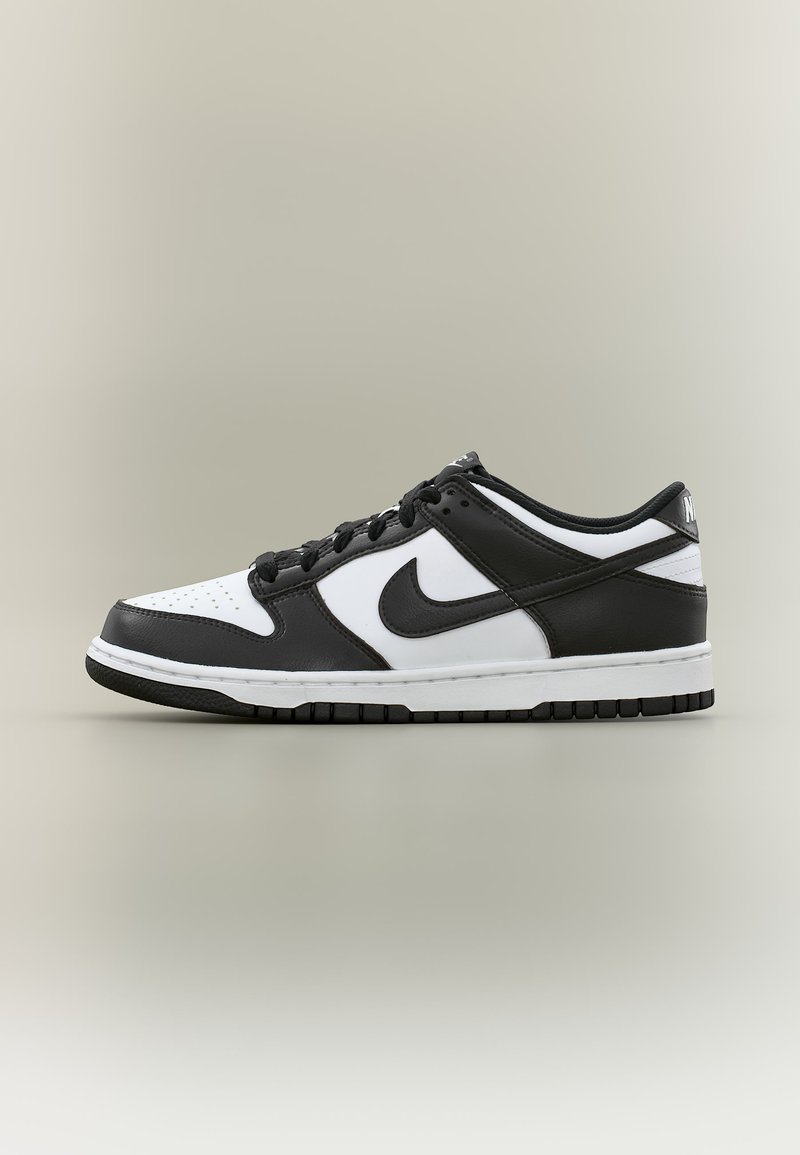 Κοντό μαύρο και άσπρο αθλητικό παπούτσι Nike με μαύρο σήμα, μαύρα κορδόνια και διάτρητο μπροστινό μέρος, παρουσιάζεται σε ουδέτερο φόντο.