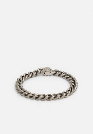 Bracelet à grosse chaîne argentée avec un fermoir solide, posé à plat sur un fond clair uni.