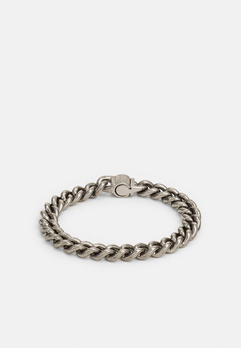 Bracelet à grosse chaîne argentée avec un fermoir solide, posé à plat sur un fond clair uni.