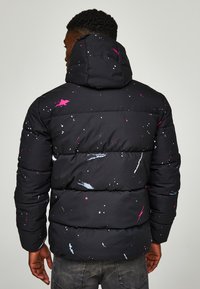 Μαύρο μπουφάν με κουκούλα, με σχέδιο πιτσιλωτού σε ροζ, λευκό και μπλε. Ραμμένο σχέδιο με απαλό, υφασμάτινο φινίρισμα.