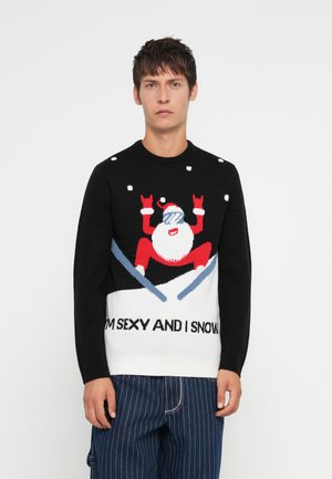 Strikkegenser med svart kropp, grafikk av en skiende nisse i hvitt og rødt, blå detaljer, og teksten "JEG ER SEXY OG JEG SNØR" langs kanten.