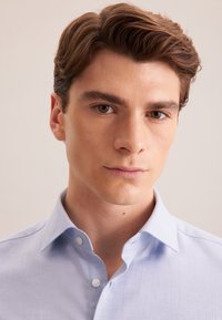 Lichtblauw overhemd met knopen en een puntige kraag, gemaakt van een gladde stof, met een subtiele textuur en standaard knoopsluiting.