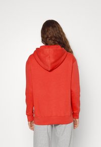 Rode hoodie met een ruime capuchon, lange mouwen en geribbelde manchetten. Gemaakt van een zachte katoenmix met een comfortabele pasvorm, gecombineerd met grijze sweatpants.