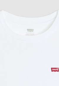 T-shirt branca de algodão com decote redondo. Apresenta um pequeno logótipo vermelho da Levi's no lado superior esquerdo, textura suave e elementos de design simples.