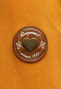 Hnědá kožená nášivka s měděným srdcovým emblémem s jemným designem. Text zahrnuje "Ragwear" a "od roku 1997" na oranžovém pozadí.