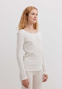 Top bianco a maniche lunghe con scollatura rotonda, realizzato in un materiale leggero con un sottile motivo testurizzato su tutta la superficie.