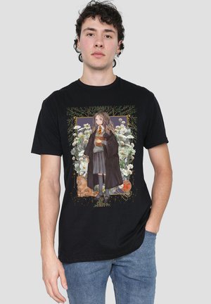 Junger Mann trägt ein schwarzes T-Shirt mit einem Anime-Mädchen in Schuluniform und Umhang, das ein Buch hält, umgeben von Blumen und einem kleinen Hund.