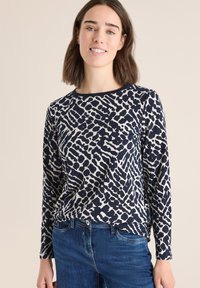 Marineblauwe lange mouwen top met een abstract lichtgekleurde patroon; ronde halslijn; zachte stof; gecombineerd met blauwe spijkerbroeken.