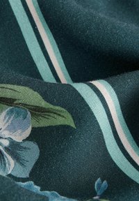 Tela con un fondo verde oscuro y patrones florales en azul y verde, acentuada por rayas verticales en azul claro y beige.