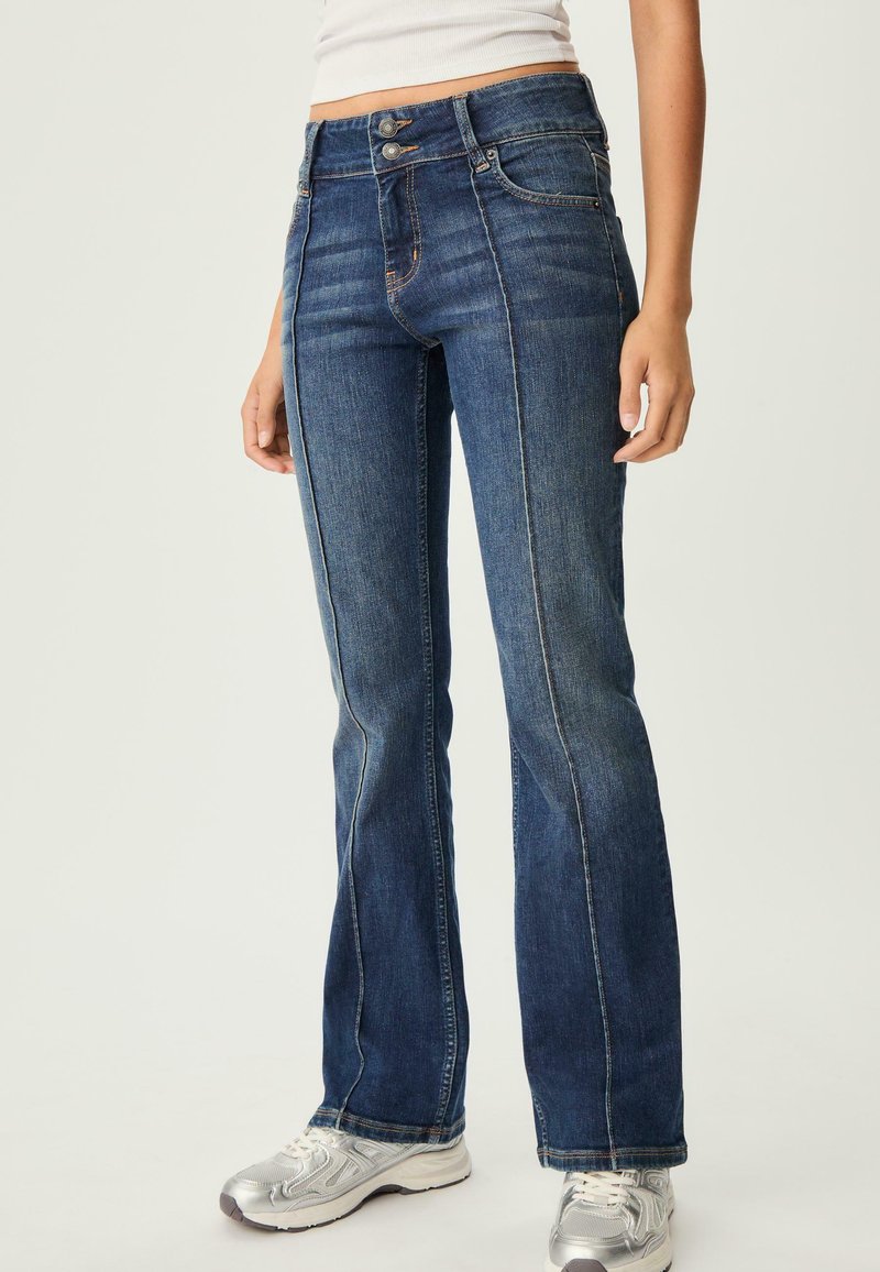 Dzwony niebieskie jeansy z denimu o średnim praniu, z wysokim stanem, dwoma guzikami i kontrastującymi detalami w stębnowaniu.