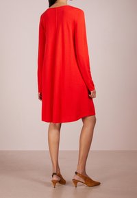 Abito rosso a maniche lunghe con una vestibilità morbida e scollo rotondo. Tessuto morbido e liscio con un orlo a metà lunghezza. Tacchi marroni con un design affusolato.