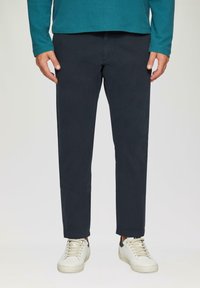 Marineblaue Chinos mit geradem Schnitt, aus einem glatten Baumwollmaterial und subtilen Stichdetails. Kombiniert mit weißen Sneakers.