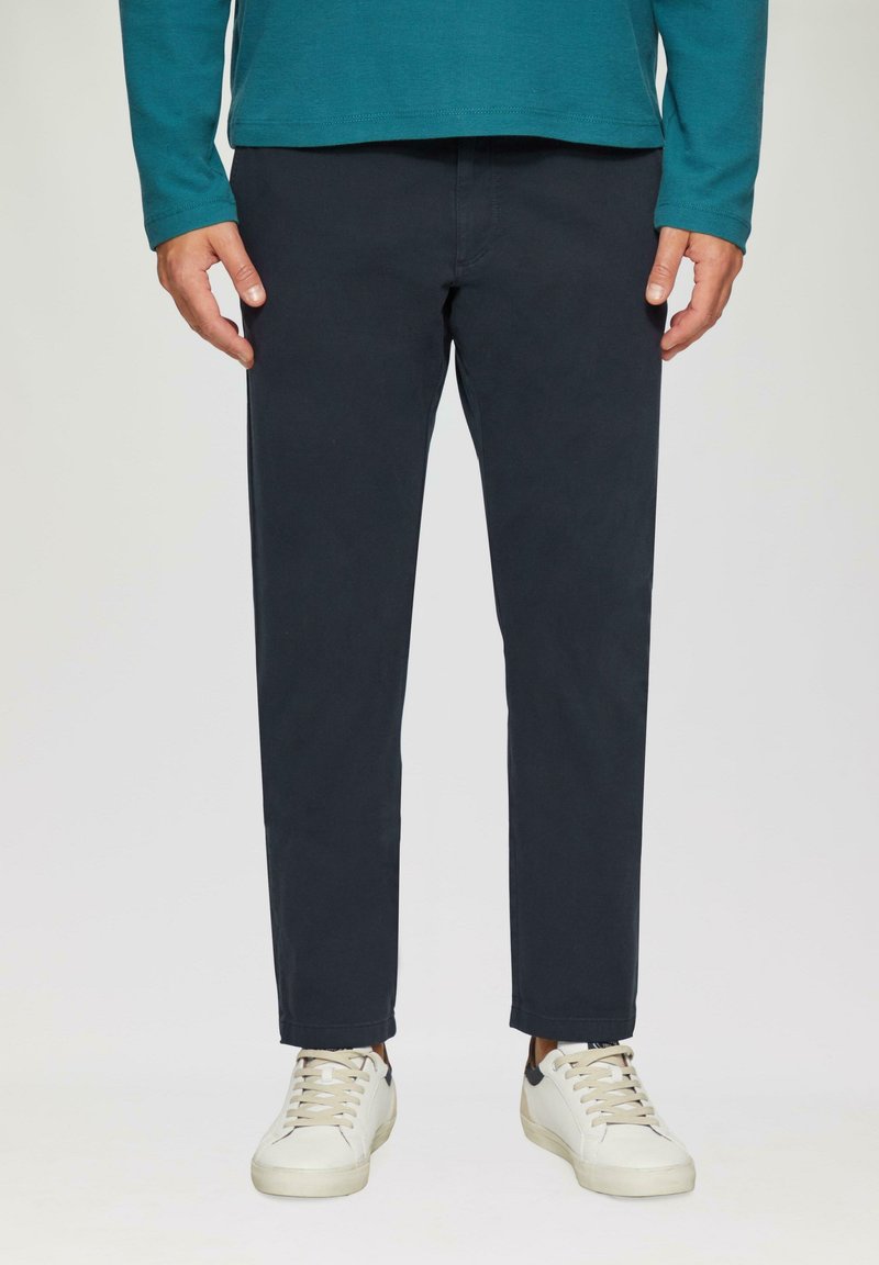 Marineblaue Chinos mit geradem Schnitt, aus einem glatten Baumwollmaterial und subtilen Stichdetails. Kombiniert mit weißen Sneakers.