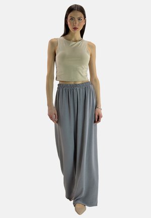 Top corto beige abbinato a pantaloni ampi grigi chiari con cintura elastica. Il modello sta in piedi con le braccia rilassate ai lati.