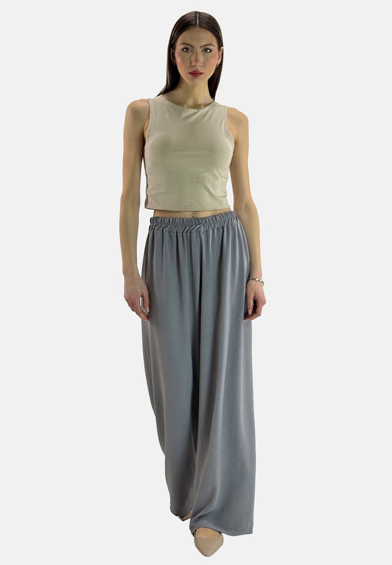 Beige korte tanktop gecombineerd met lichtgrijze wijde broeken met een elastische tailleband. Model staat met ontspannen armen langs het lichaam.