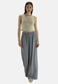 Lysebeige croppet tanktop, kombineret med løse, grå, højtaljede bukser. Glat tekstur, afslappet pasform, minimal detaljer og ankel-længde.