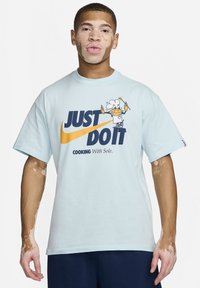 T-shirt en coton bleu clair avec un grand graphisme portant "JUST DO IT," un chef en dessin animé, et "COOKING With Sole" en dessous en bleu foncé. Manches courtes.