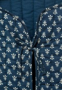 Zblizu prikazan mornarsko moder prešit tekstil z belim simetričnim cvetličnim vzorcem, z vezano tkaninsko pentljo na srednji šiv.