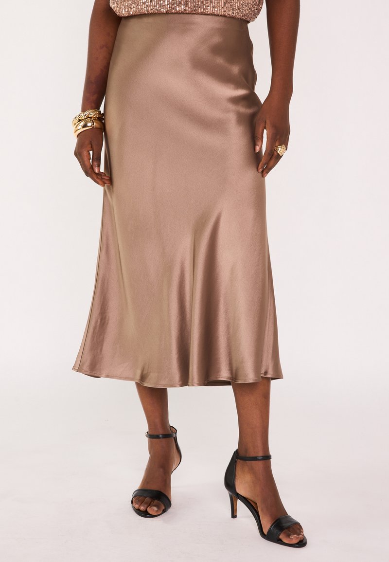 Gonna di media lunghezza in satin bronzo con texture liscia e orlo svasato, abbinata a sandali neri con tacco alto e cinturini.