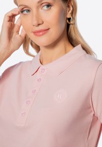 Růžová polo tričko s texturovanou tkaninou, se límečkem, šesti knoflíky a vyšívaným logem na hrudi.