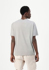 Camiseta de algodón gris con mangas cortas y cuello redondo, que presenta una textura suave y un corte holgado, combinada con pantalones cortos beige claro.