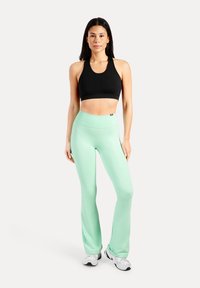 Haut de sport court noir, leggings taille haute vert menthe, texture lisse, design ajusté, assortis à des baskets blanches.