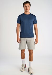 Mørkeblå kortærmet t-shirt lavet af glat, letvægtsstof, parret med grå atletiske shorts. Sneakers med accenter fuldender looket.