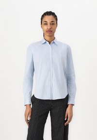 Camicia a maniche lunghe a righe azzurro chiaro con collo alla camicia, presenta un piccolo logo ricamato sul lato sinistro del petto. Pantaloni a righe nere.